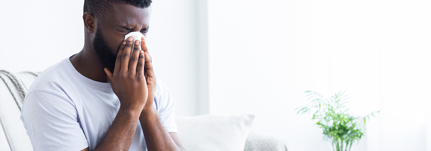 A person sits on the couch blowing their nose.