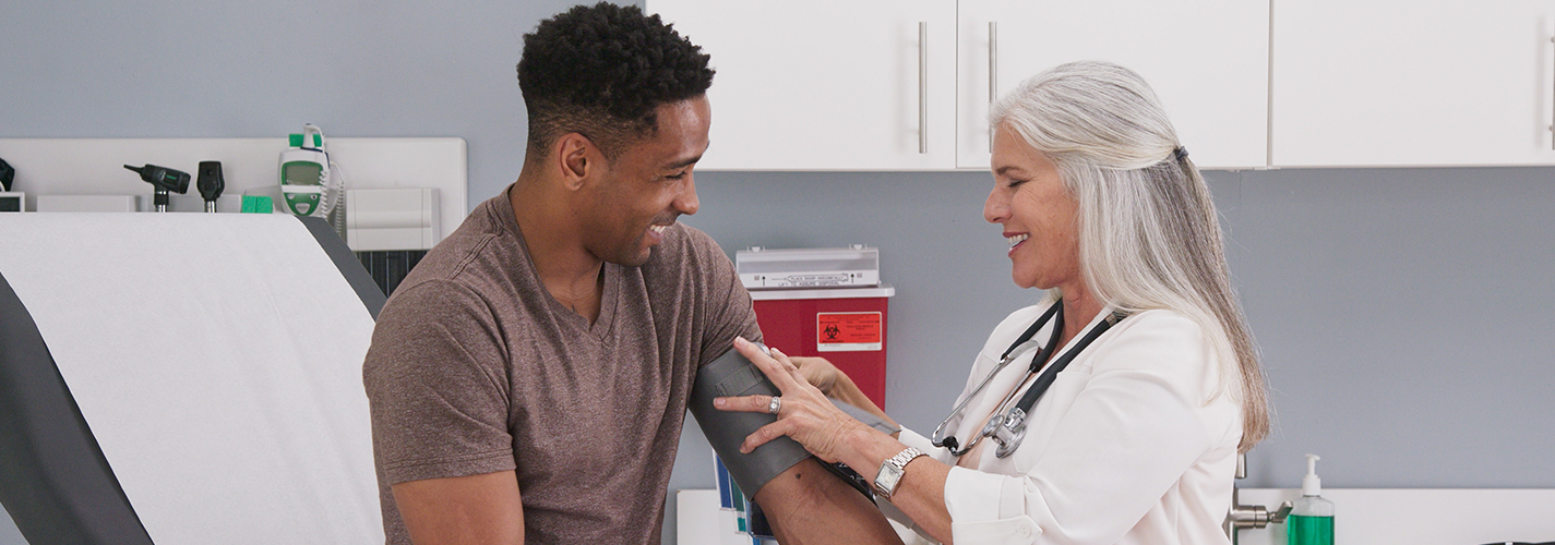 A doctor checks the blood pressure of a smiling patient.