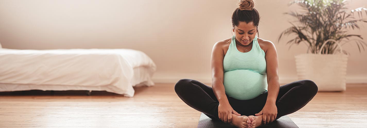 A pregnant woman does yoga in her living room.