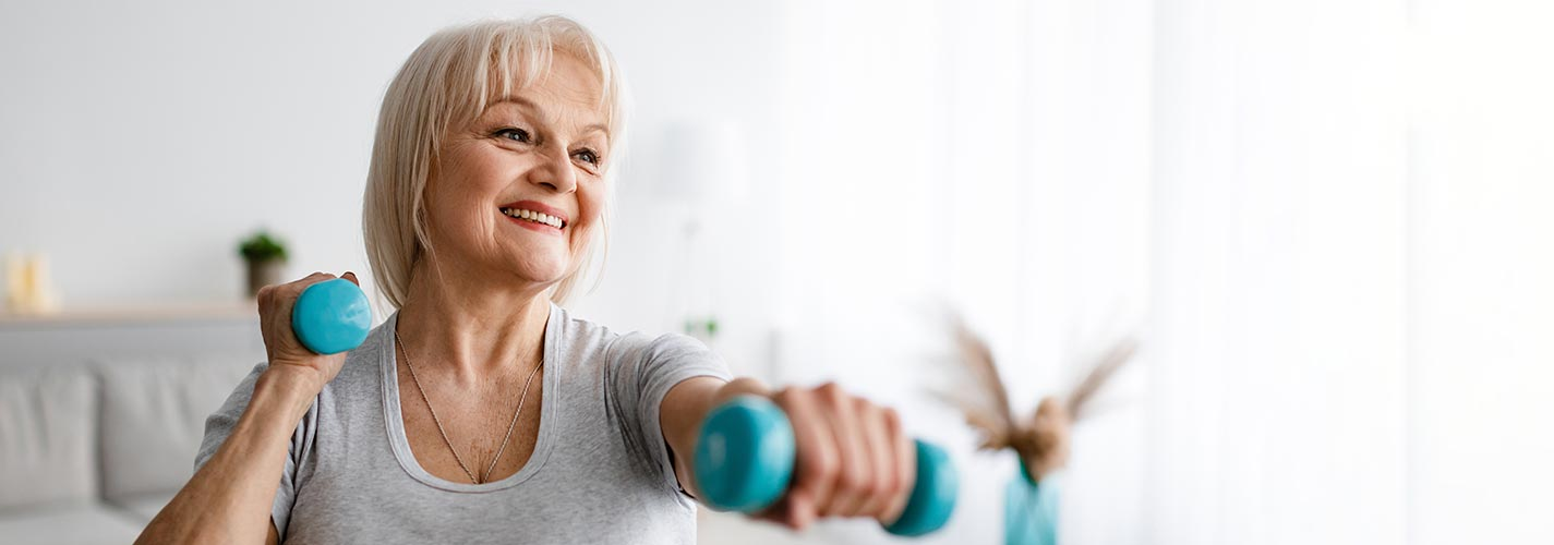 An older woman smiling as she exercises with teal five pound weights.