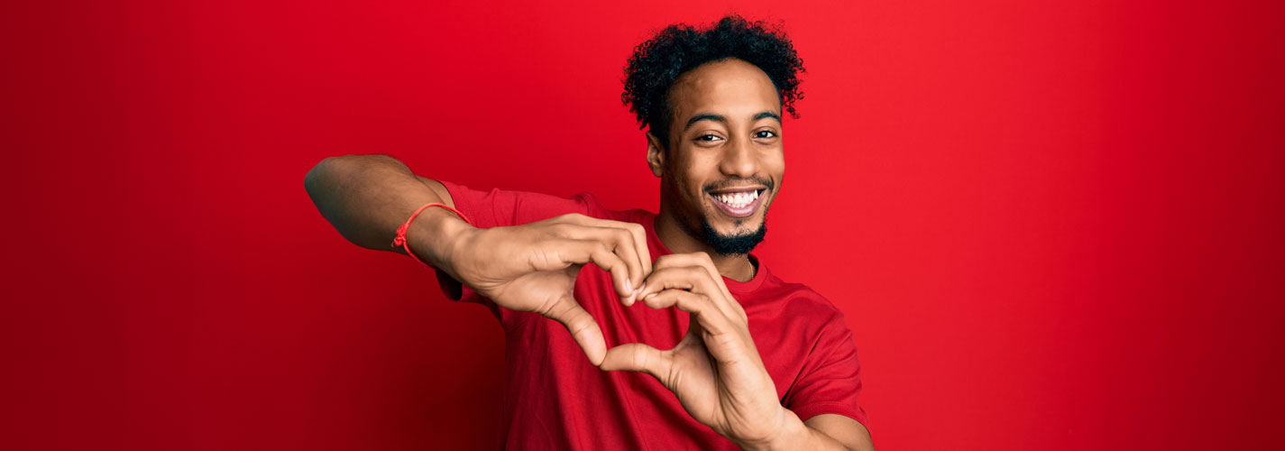 Young African American man wearing a red t-shirt and making a heart symbol with his hands.