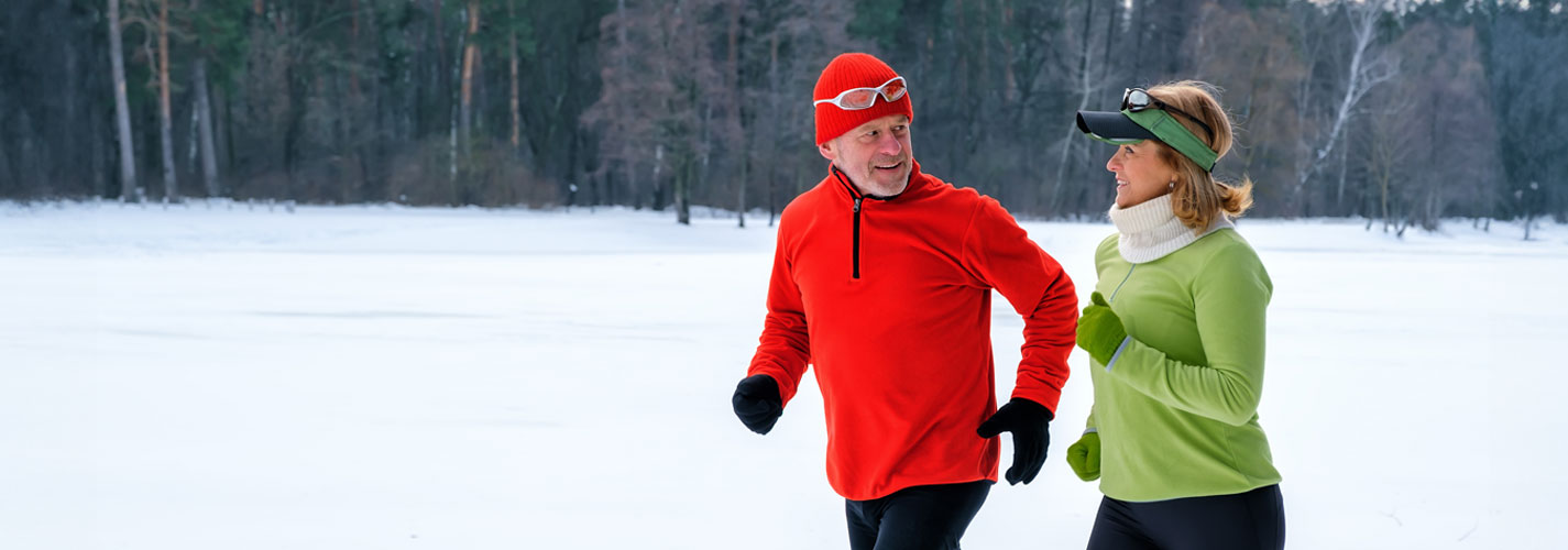 A smiling senior couple jogging in a snowy winter park.