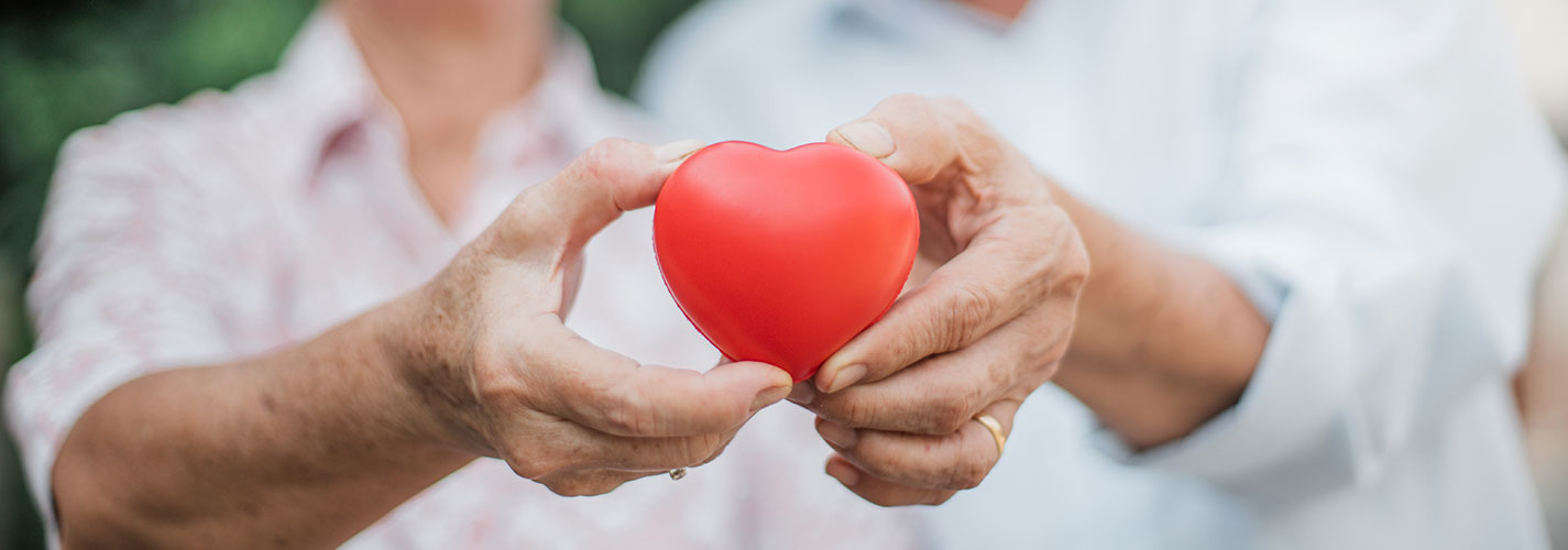 Happy mature couple holding a red heart in front of a lovely background.