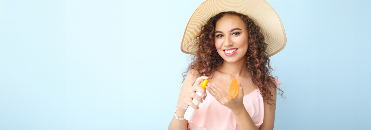 Happy African-American woman with sunscreen cream on a sky blue color background.