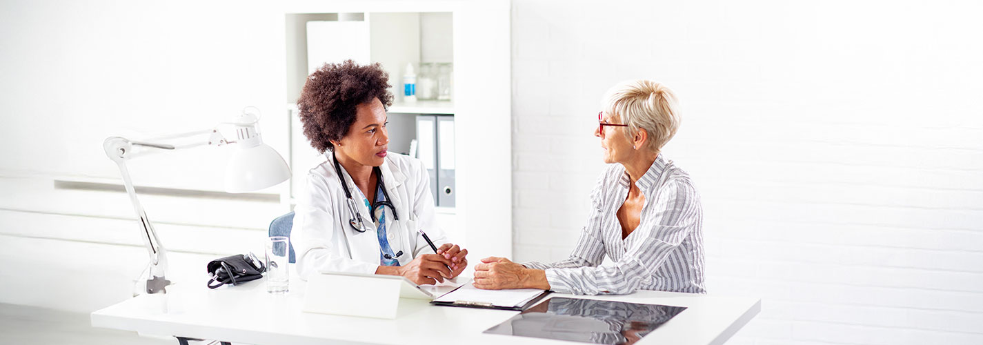 A mature woman sits at the doctor's office talking with her physcian.
