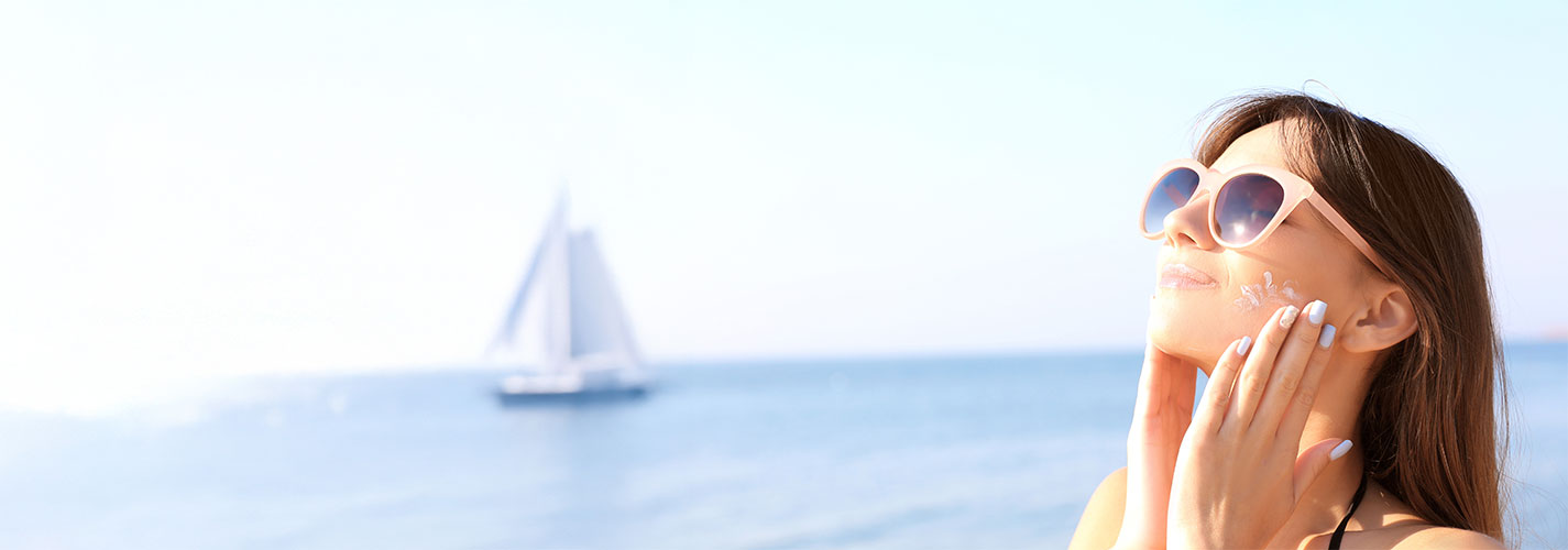Young woman using sunscreen with the sea in the background.