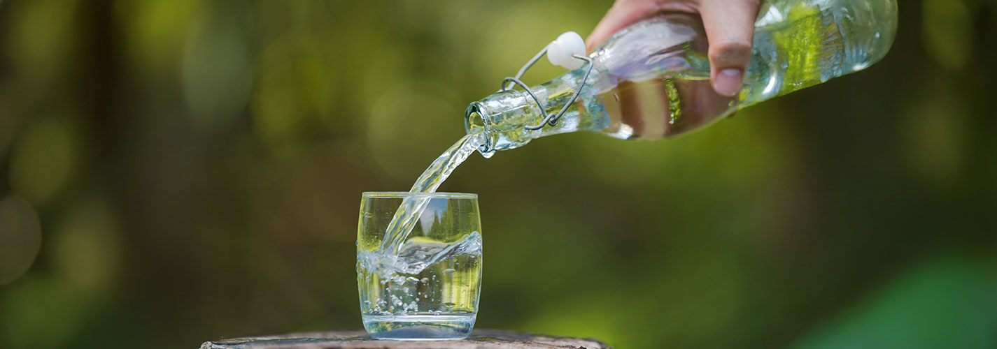 A close-up of a hand pouring some water into a glass cup.
