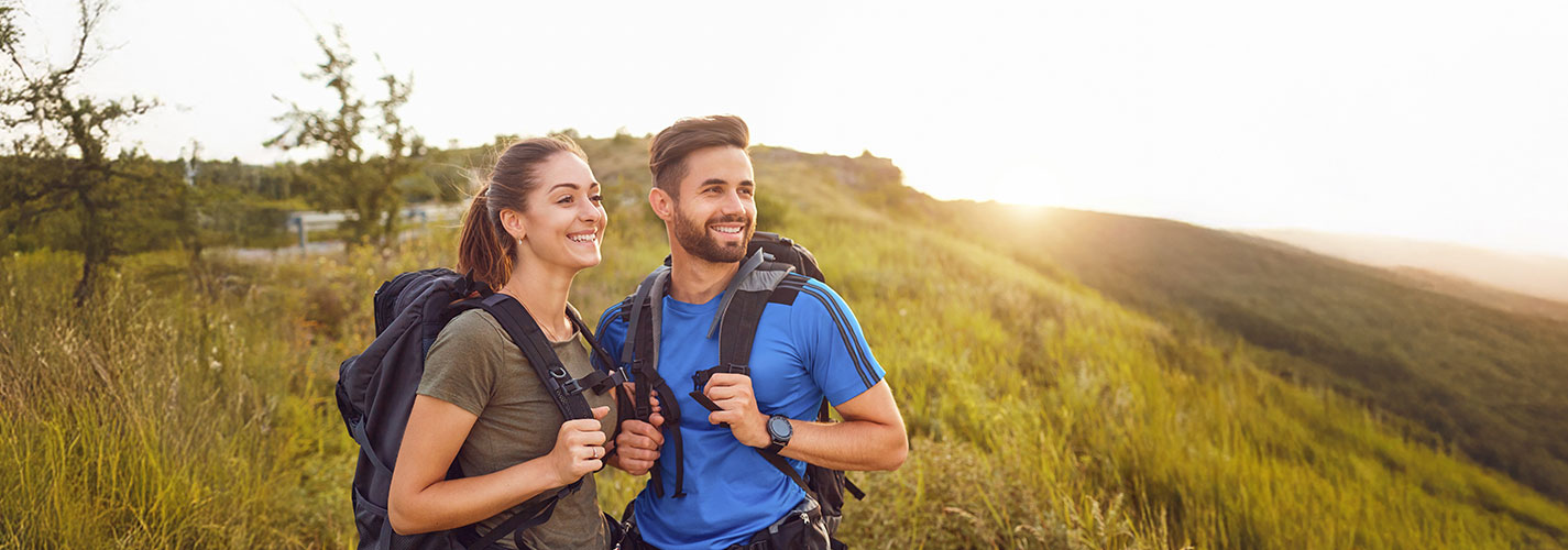 Smiling couple hiking through sunlit hills, embracing the outdoors and the journey together.