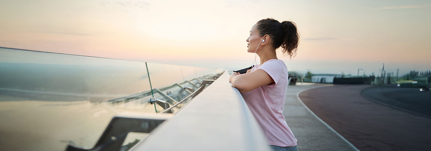 Woman enjoying a peaceful morning moment after exercise, listening to music, and taking in the sunrise view.