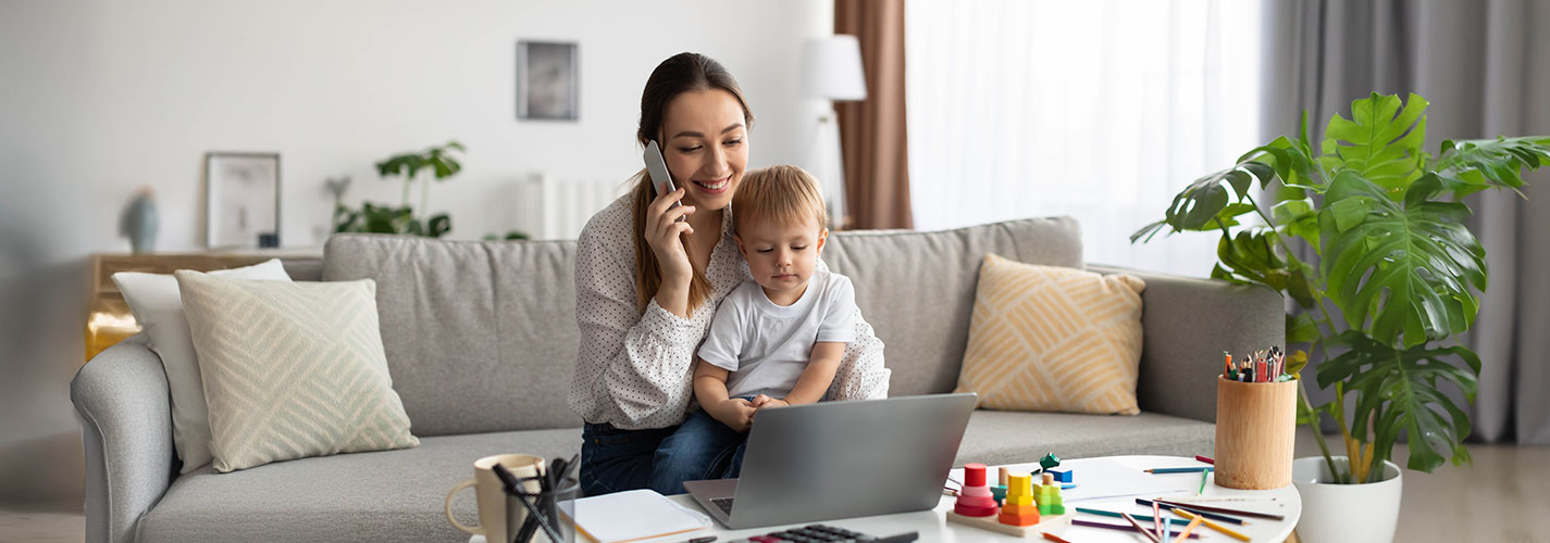 Woman working from home with a child on her lap, talking on the phone.