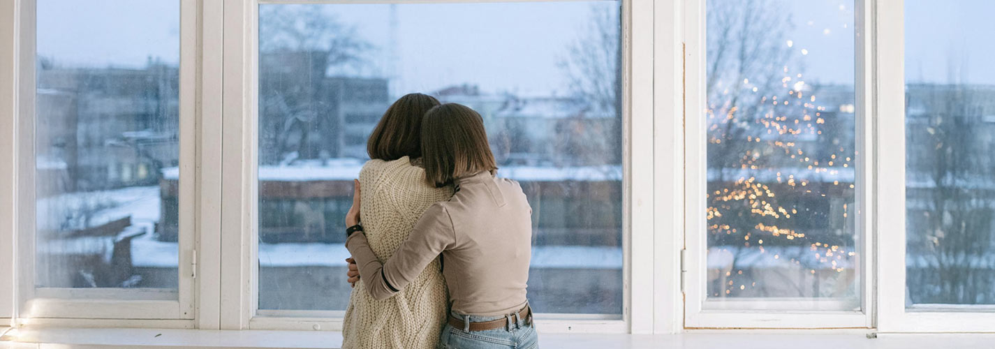 Two people hugging while looking out a large window at a snowy cityscape.