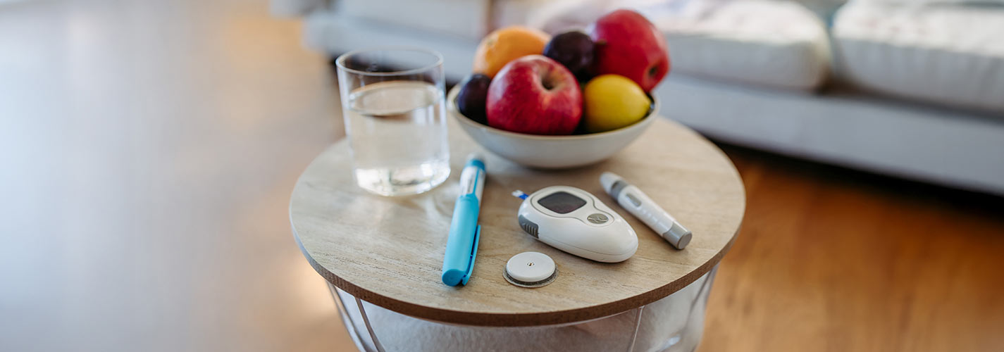 A close-up of diabetes supplies and devices on a table next to a bowl of fruit.