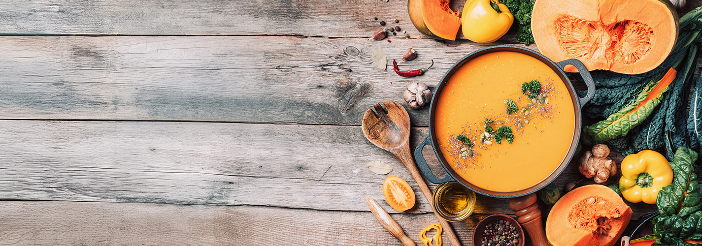 Top view of pumpkin soup surrounded by healthy autumn vegetables.