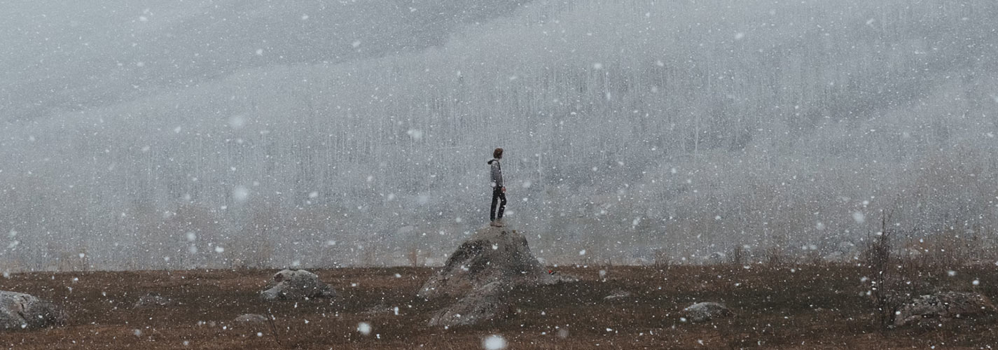 A person stands alone on a rock in a snowy wintery landscape.